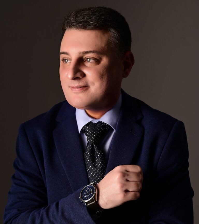 Retrato profissional do Ricardo Rios com terno azul escuro e gravata, de perfil leve, braços cruzados, fundo transparente.